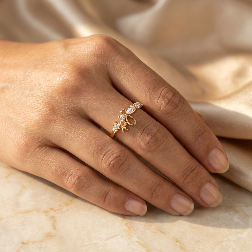 Adult hand wearing a gold-tone clear-stone ring with loop detailing while holding champagne fabric.
