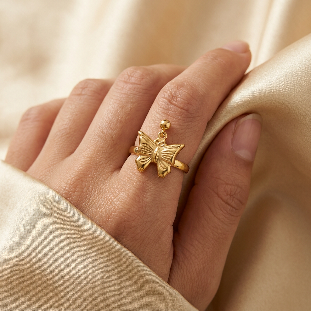 Adult hand wearing a gold-tone butterfly ring while gently holding champagne satin.