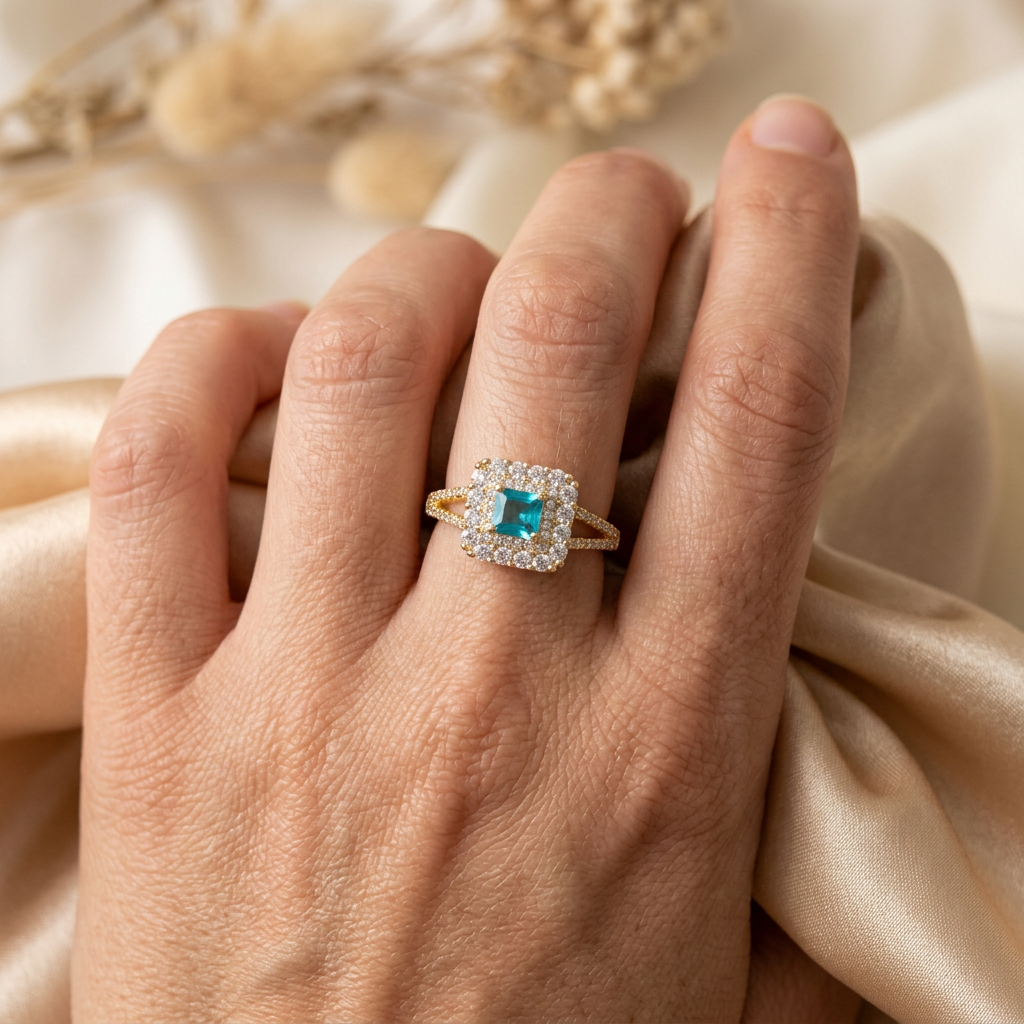 Aquielle aqua rectangular halo ring worn on an adult hand gently gathering champagne satin