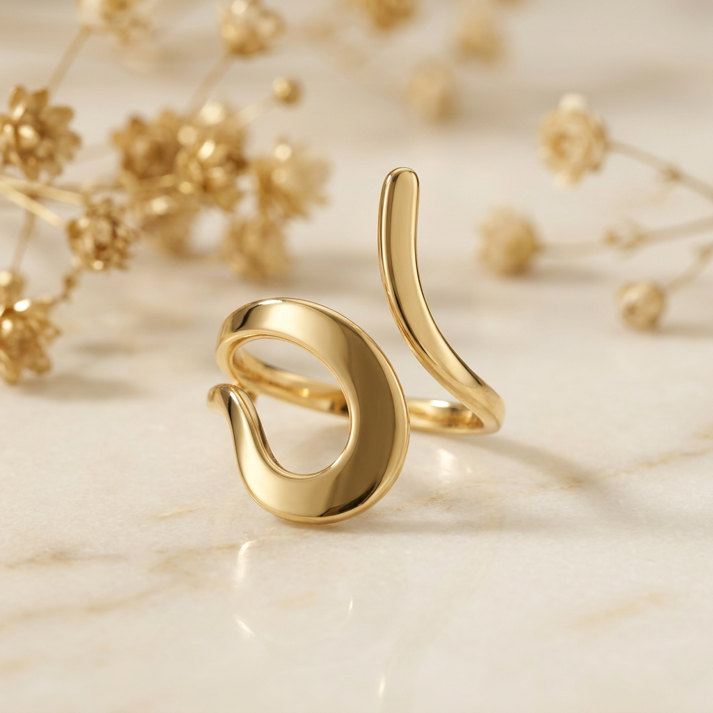 Gold-tone curl open-front ring on cream marble with blurred golden florals.