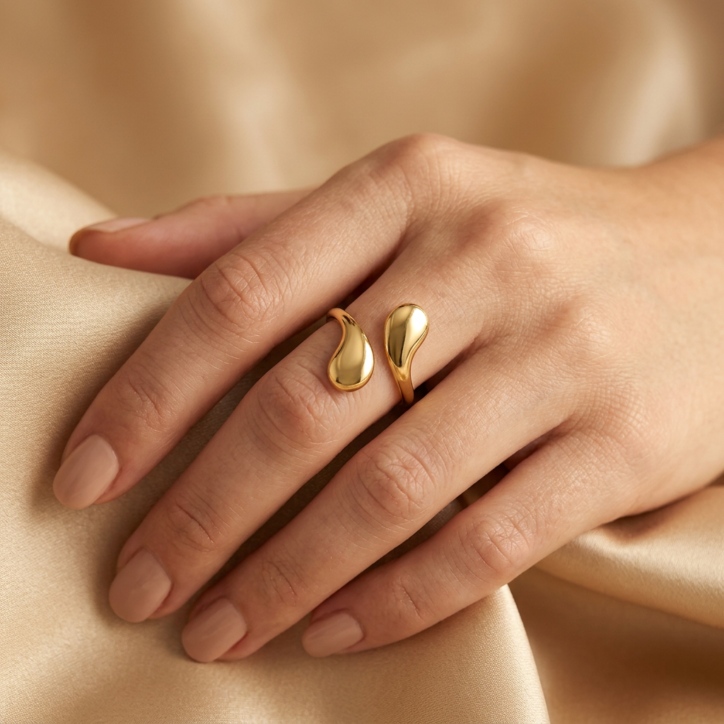 Adult model wearing gold-tone teardrop ring while holding champagne satin.
