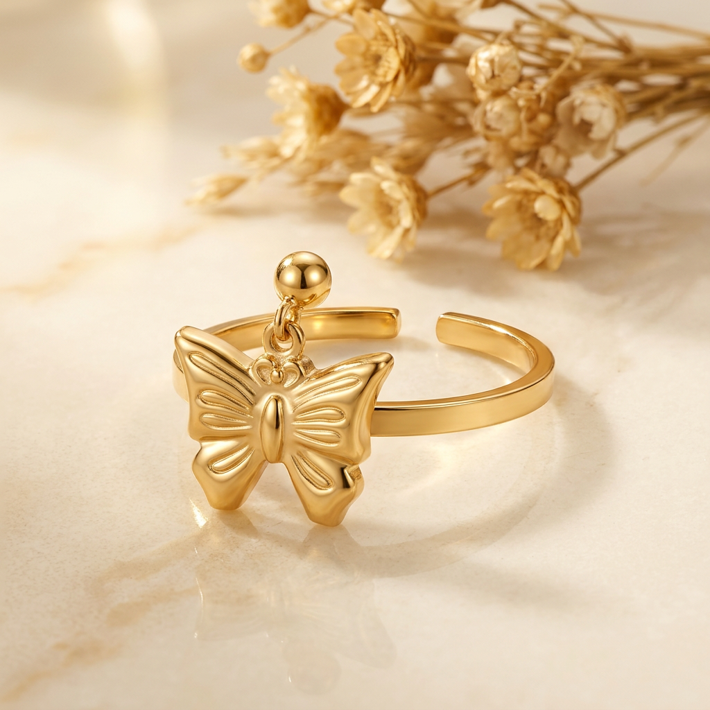 Gold-tone butterfly ring with bead accent and open rear band on cream marble with blurred golden florals.