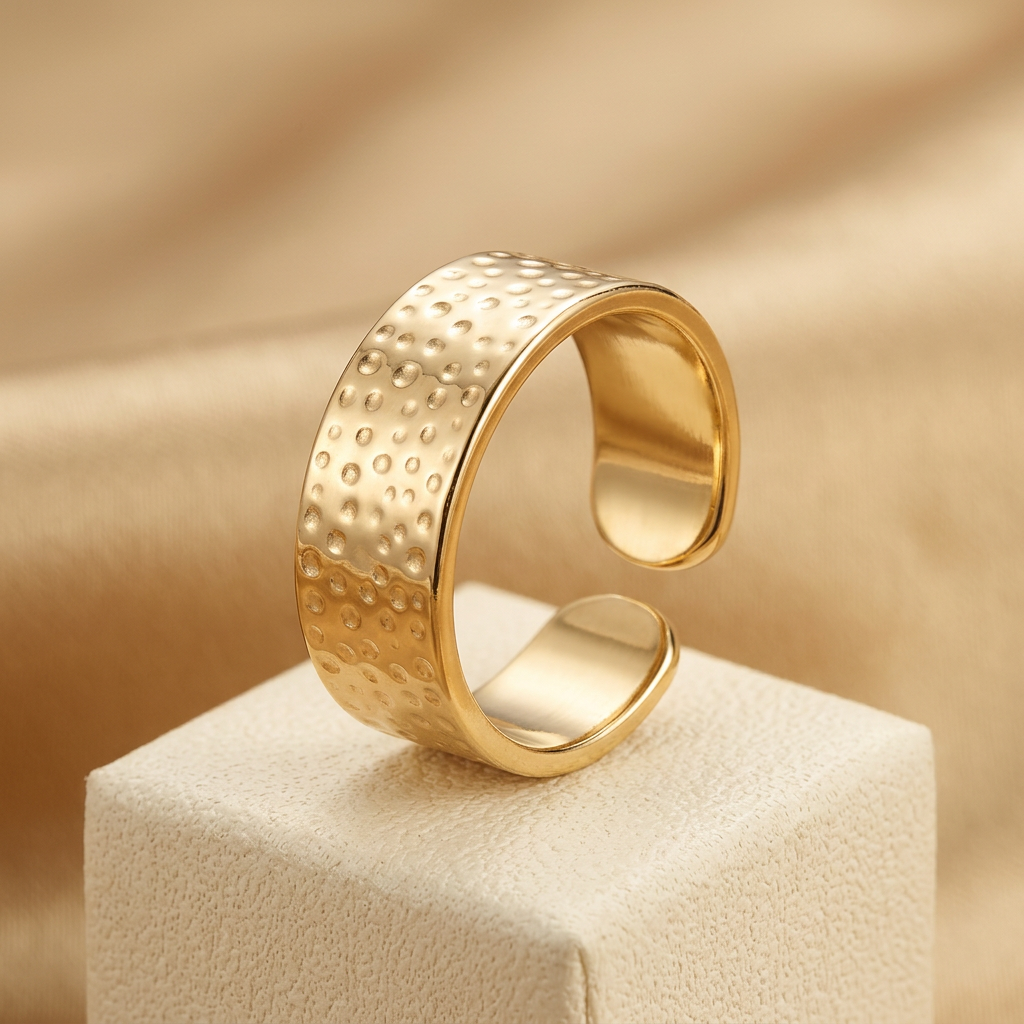Open-back gold-tone hammered ring on cream pedestal.