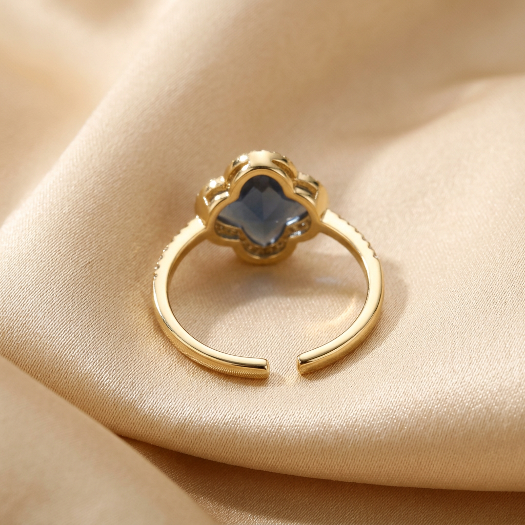 Rear construction view of blue quatrefoil ring showing separated free-size band ends on champagne fabric.