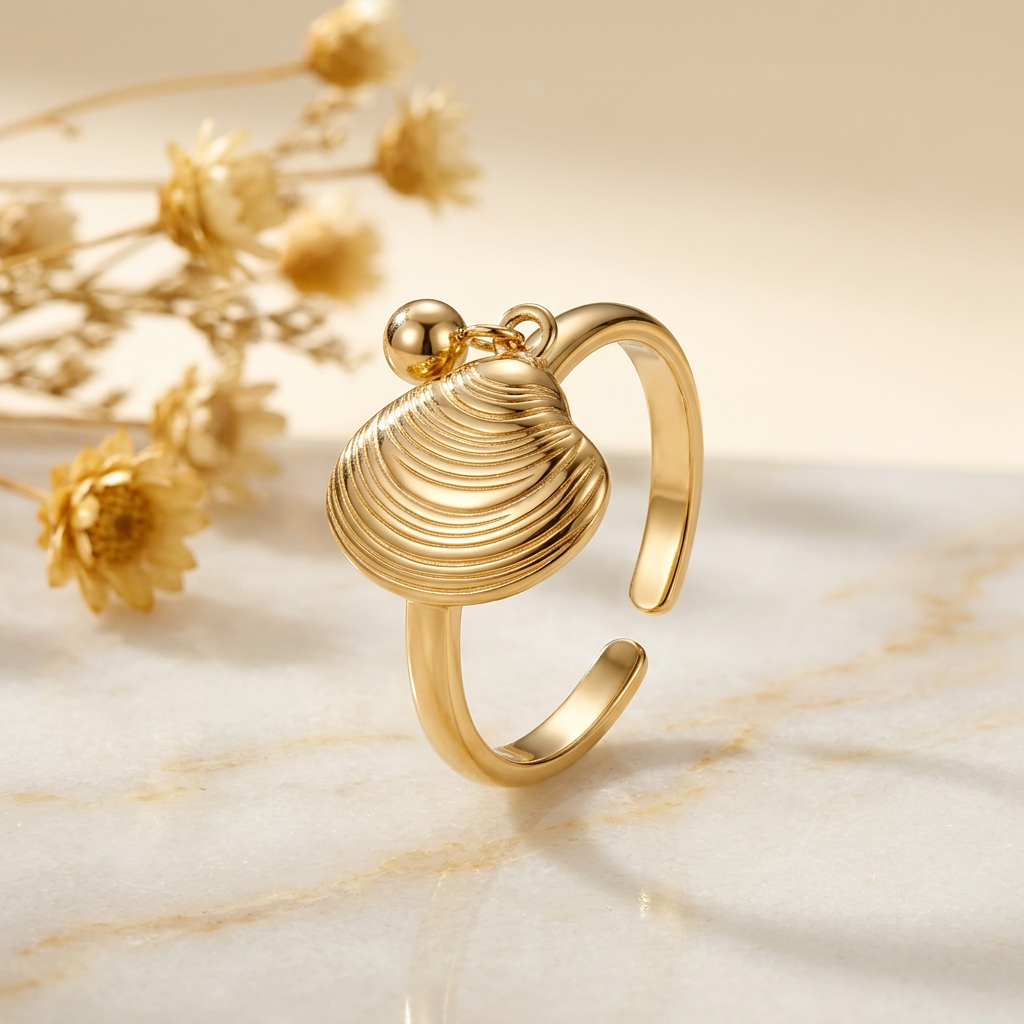 Gold-tone ridged shell ring on cream marble with softly blurred golden flowers.