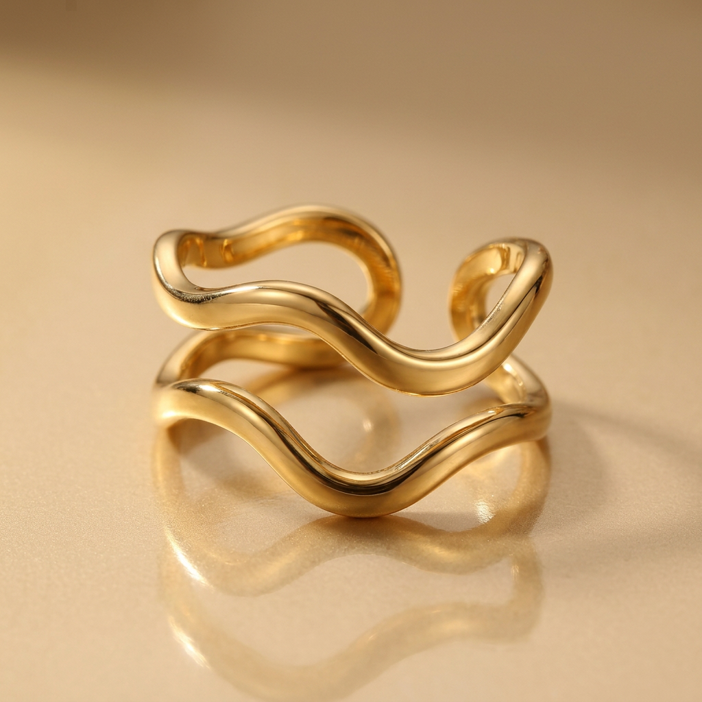 Close-up of gold-tone double-wave ring on a champagne-gold surface.