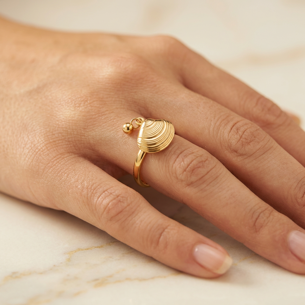 Adult model wearing gold-tone shell ring with hand resting on cream marble.