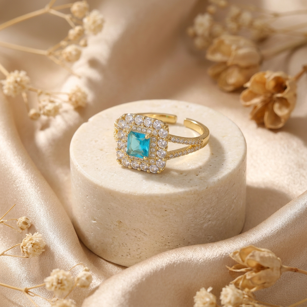 Aquielle aqua halo ring on a cream stone pedestal surrounded by champagne satin and dried flowers