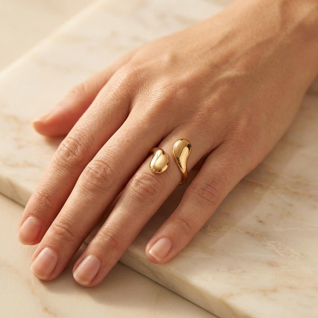 Adult model wearing gold-tone teardrop open ring with hand resting on cream marble.